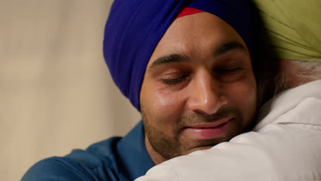 Close-Up-Studio-Shot-Of-Adult-Sikh-Son-Embracing-Senior-Father-Both-Wearing-Turbans-Against-Plain-Background